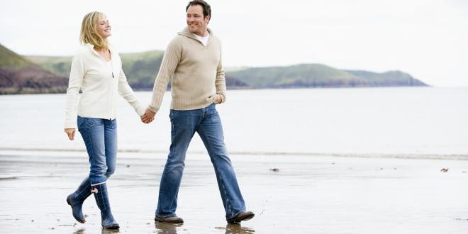 a middle-aged couple holding hands while they walk down a rugged beach